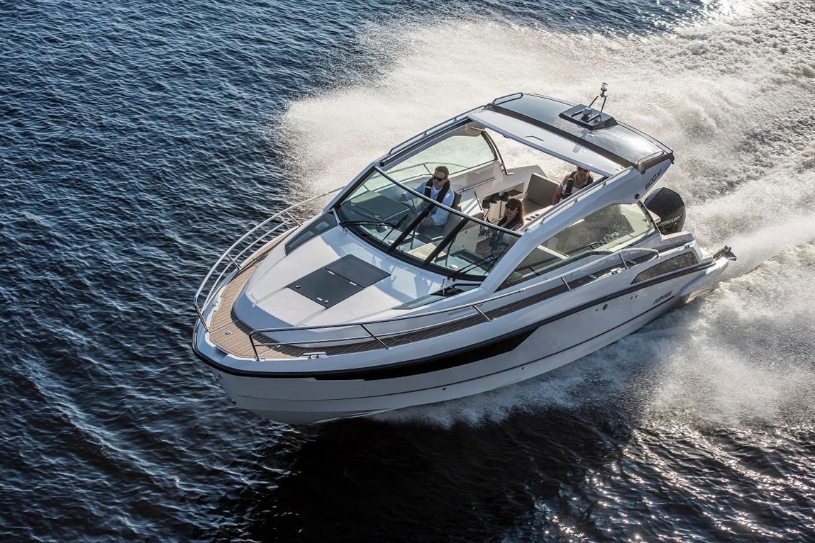 Luxury motorboat cruising on water, with two people visible in the cockpit, leaving a wake behind.